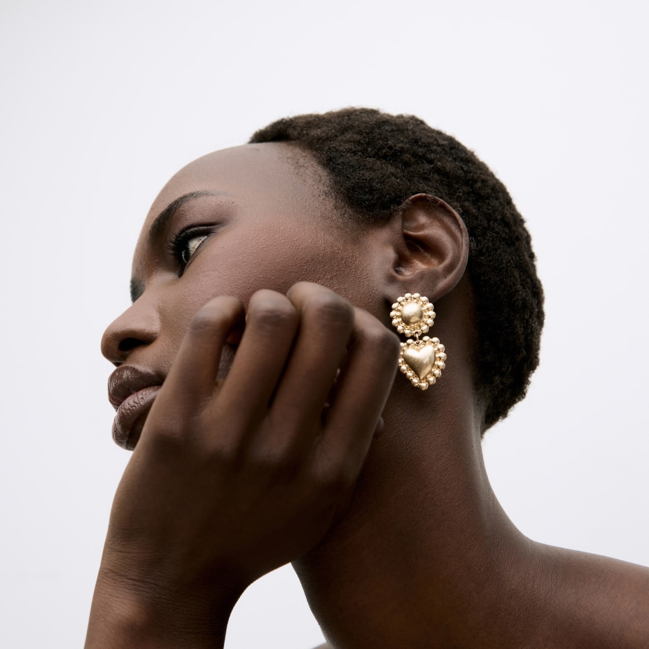 Model wearing a pair of gold drop heart earrings with scalloped edging 